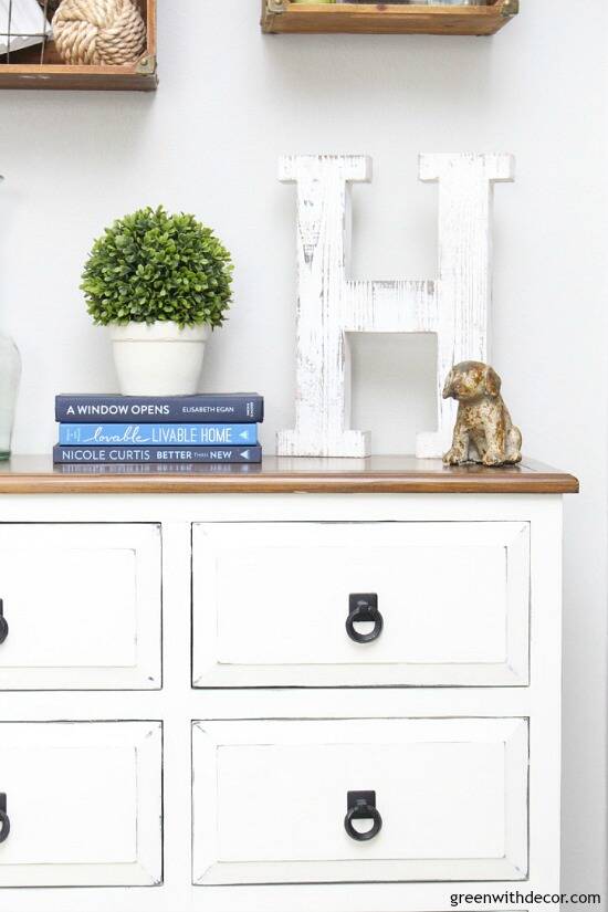 A white dresser with blue books, a plant and a ceramic dog on top