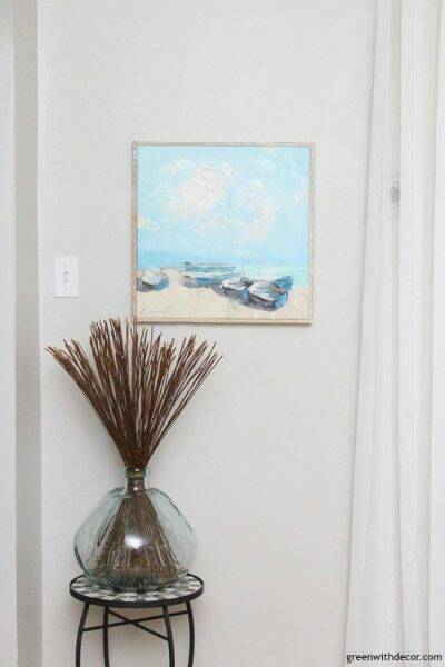 A coastal glass aqua vase and beachy artwork on a gray wall