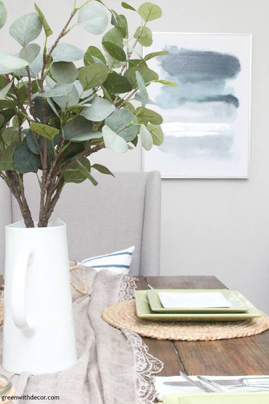 How to find your decorating style – a white pitcher of eucalyptus on a table with blue and gray artwork on the wall