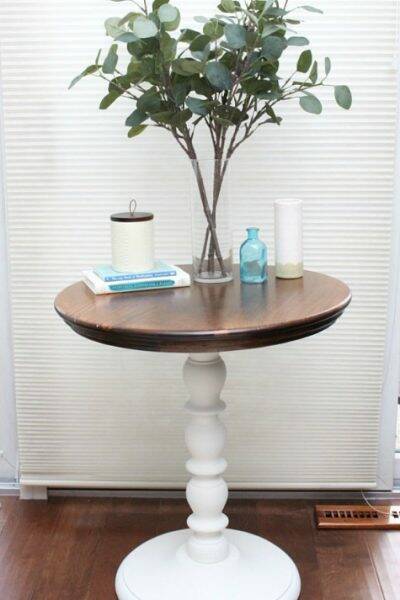 A two-toned round table with a white base and wood top with eucalyptus and white and aqua pieces on top