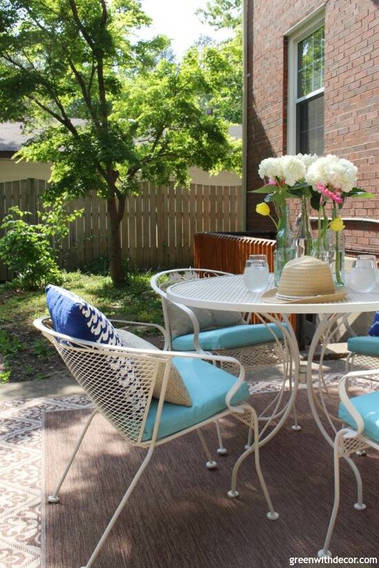 A tan metal patio set with aqua cushions, pillows and a flower centerpiece