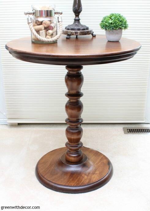 A wood round table with a lamp, greenery and corks on top.