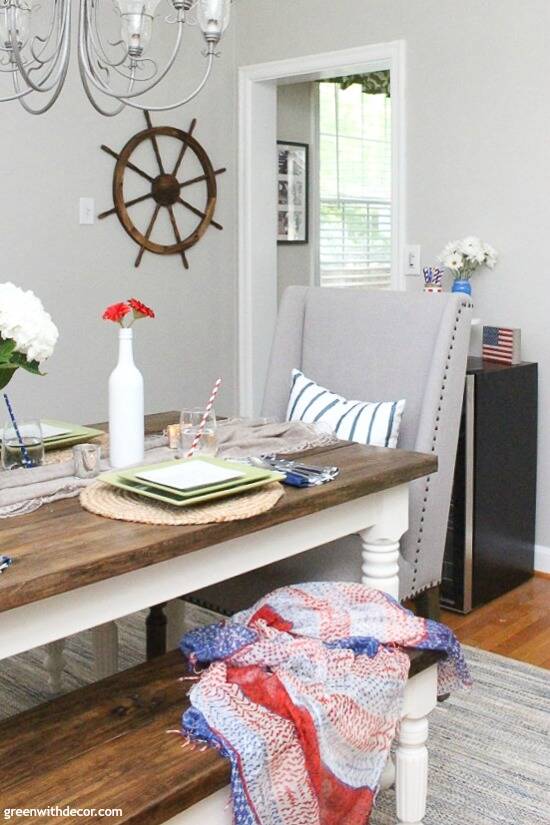 A Fourth of July table with a patriotic scarf on the bench and ship wheel on the wall