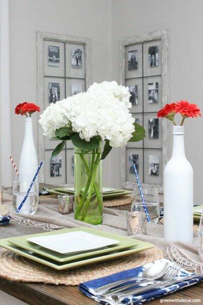 A Fourth of July table with white hydrangeas in a green vase and red flowers in white bottles