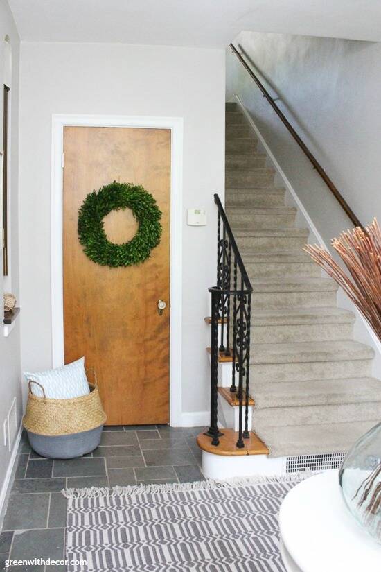 Gray coastal foyer with a slate floor, boxwood wreath, seagrass basket and tan carpeted stairs