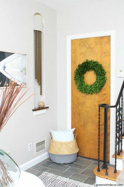 Gray coastal foyer with a wood door, boxwood wreath, boat artwork and seagrass basket