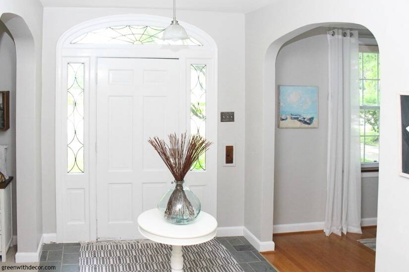 Gray coastal foyer with a white front door, white round table and aqua vase with brown sticks