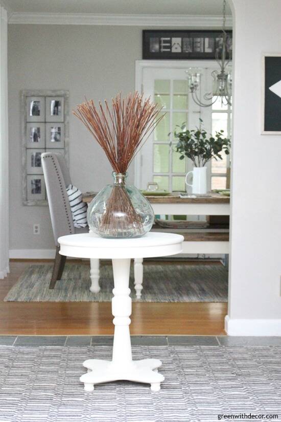 Gray coastal foyer with a white round table with an aqua vase on top, with a view into the dining room