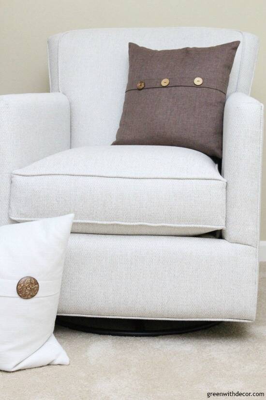 A neutral glider with brown and white throw pillows, near tan walls and tan carpet