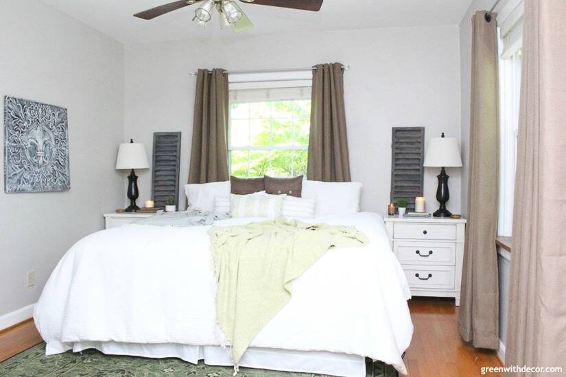A gray bedroom with white bedding, brown curtains, a green rug and green blanket