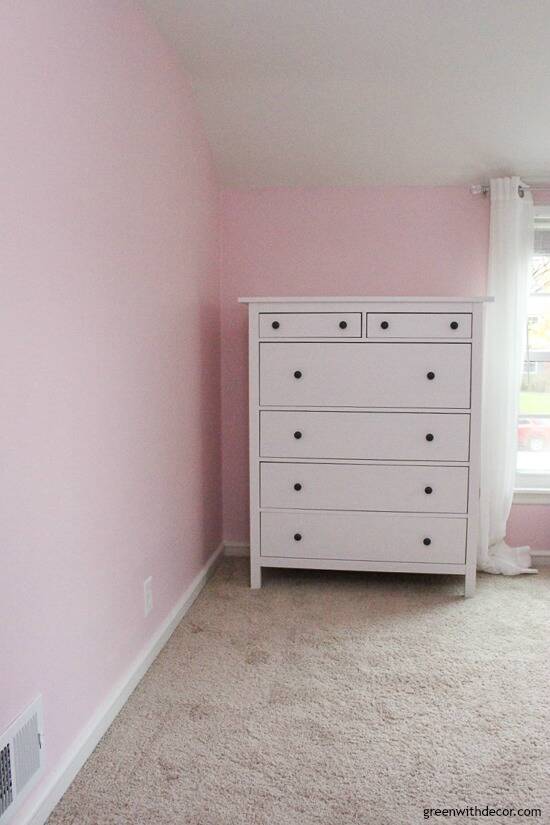 A pink nursery with a white dresser