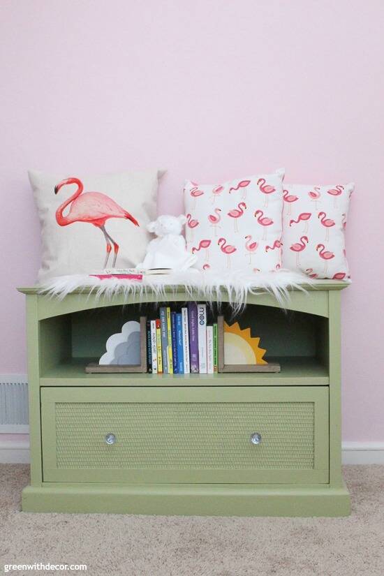 A green TV stand turned book storage in a pink nursery