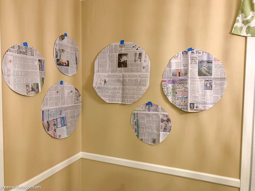 Tan dining room walls with newspaper pieces laid out for a seagrass basket gallery wall