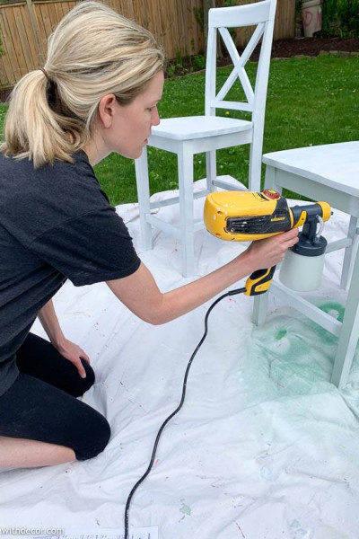 A girl using a paint sprayer to paint barstools