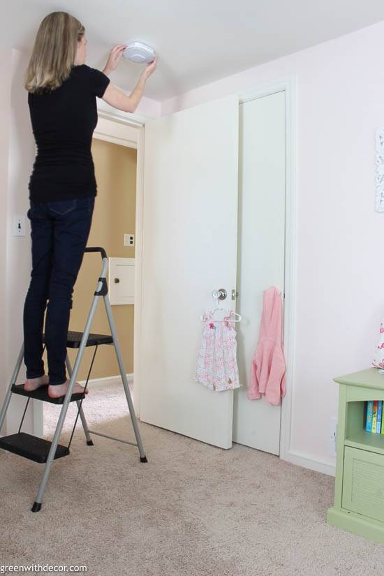 Girl installing smoke alarm in a pink nursery