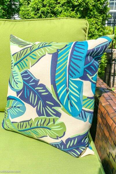 Green and blue banana leaf outdoor pillow on a green couch