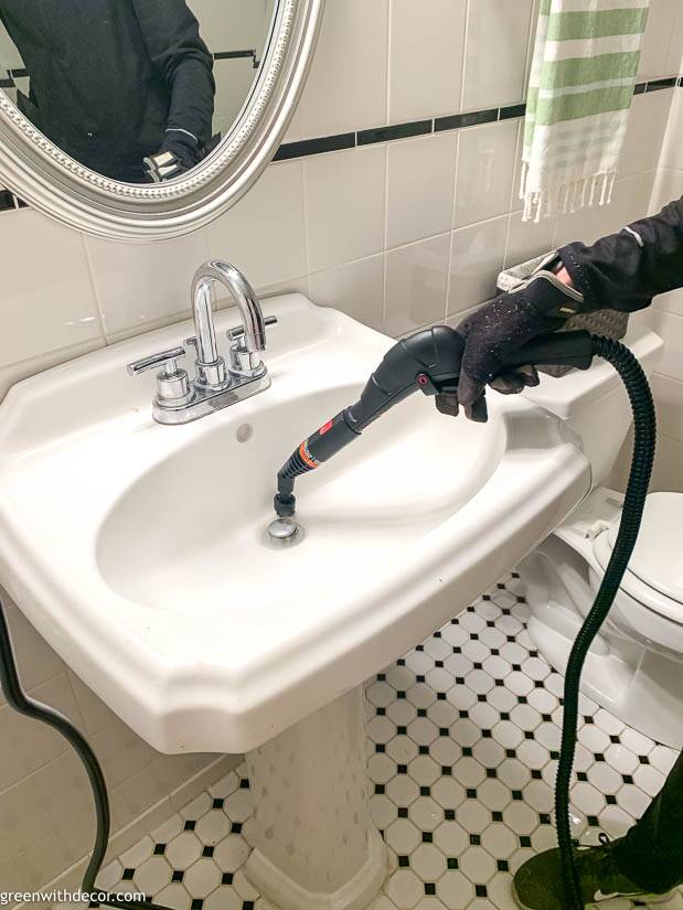 Steam cleaner being used to clean a white bathroom sink