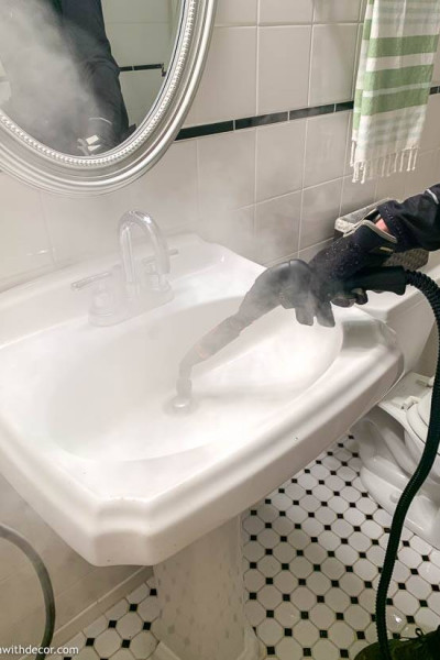 Steam cleaner cleaning a white bathroom sink