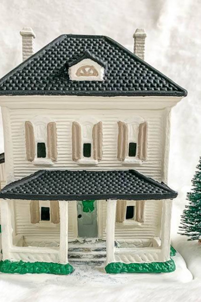White painted Christmas village house with black roof, white chimneys and tan shutters