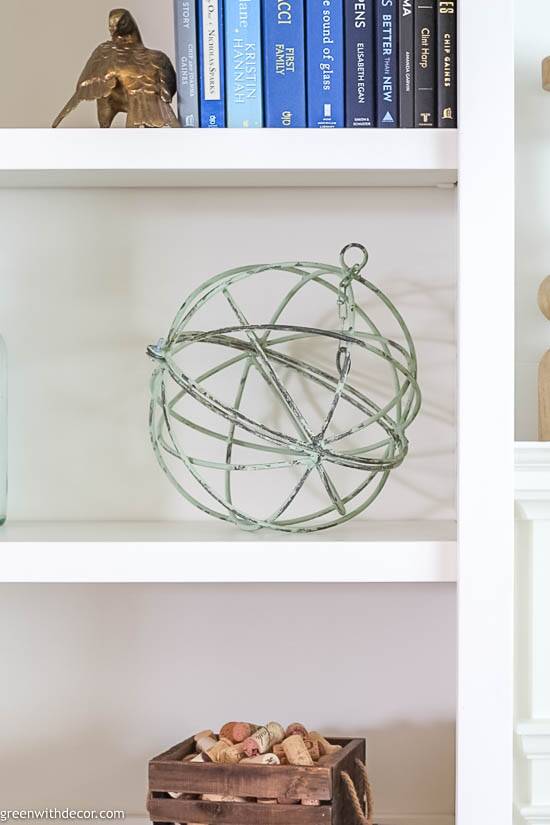 Bookshelf decorating ideas: green metal sphere, blue books and a crate full of wine corks