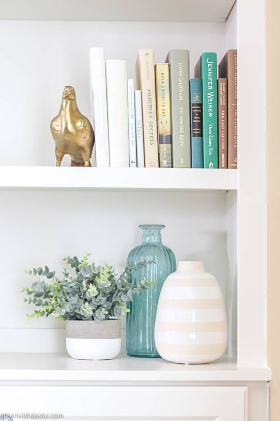 Ideas para decorar una estantería: libros neutros, sujetalibros de metal y jarrones de color aqua y blanco