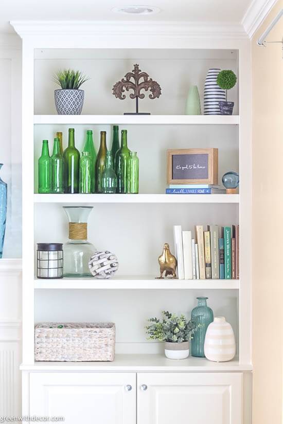 White decorated bookshelves with green bottles, blue vases and neutral books