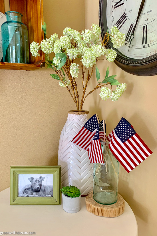 American flags in an aqua vase near a white + wood vase